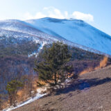 雪が積もった黒い溶岩砂利の登山道の先に、真っ白に雪化粧した浅間山と青空