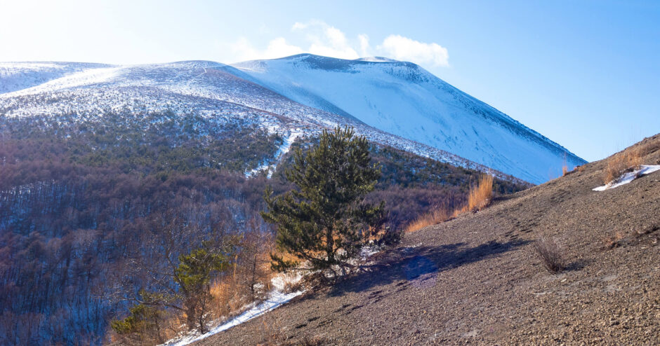 雪が積もった黒い溶岩砂利の登山道の先に、真っ白に雪化粧した浅間山と青空