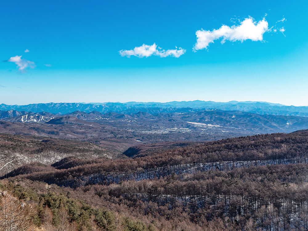 小浅間山の山頂から見下ろす、雪景色の軽井沢の街並みと遠くの山々