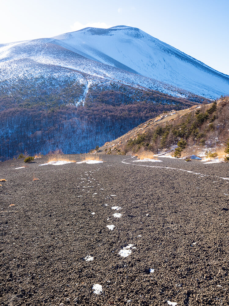 真っ白な雪の斜面に一筋続く、登山者の足跡と遠くにそびえる冬の浅間山